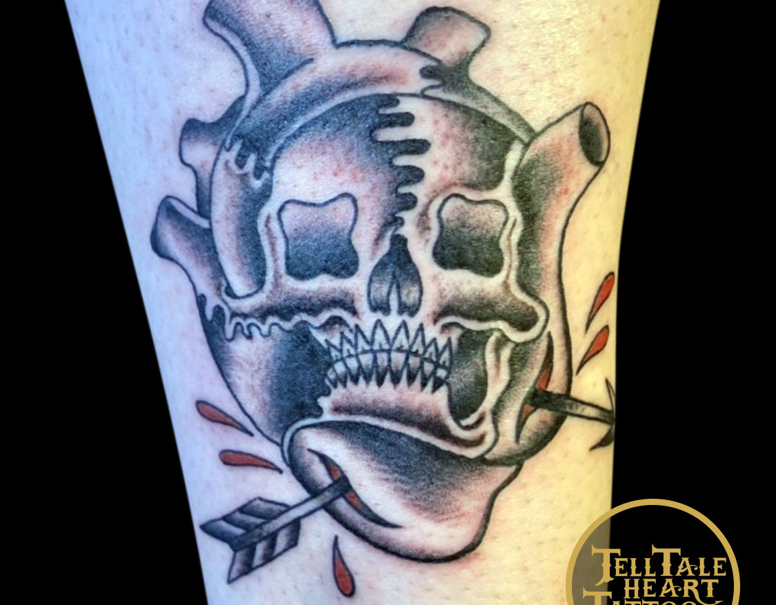 anatomical heart tattoo with a skull design inside tattooed in a traditional style with an arrow piercing the bottom and red blood drops