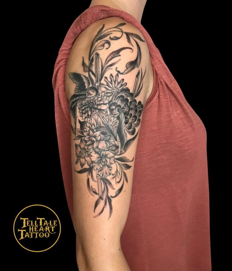 Black and grey tattoo of flowers and ornamental leaves with a swallow tattooed on outside shoulder down to elbow