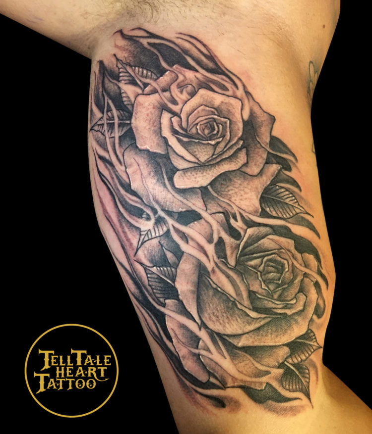 black and grey tattoo of two roses with petals and negative space flames throughout on inside bicep