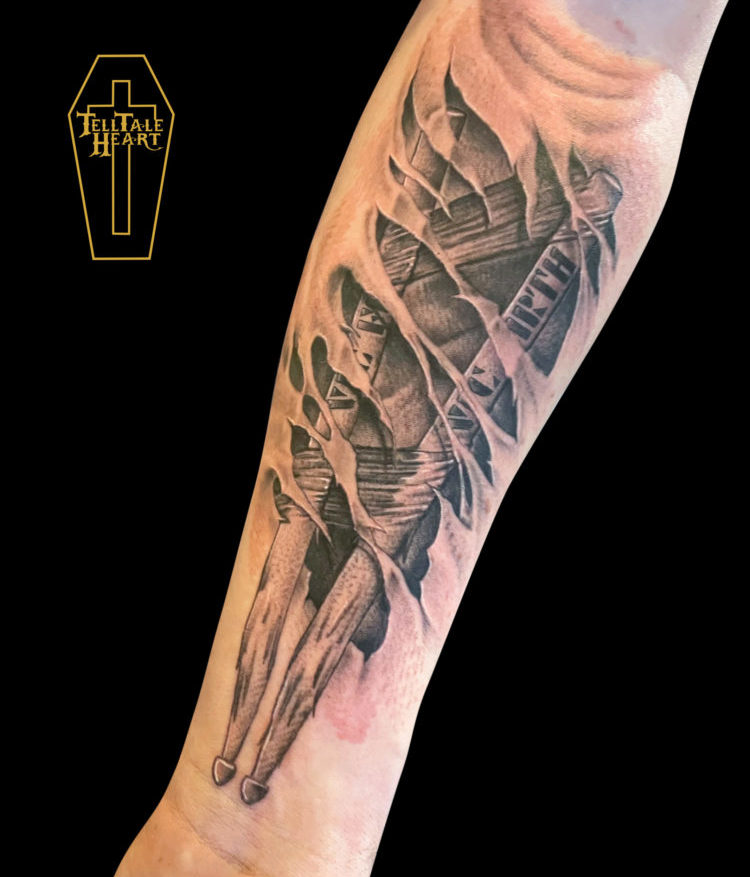 black and grey realism tattoo of a pair of drum sticks coming out of torn skin on forearm