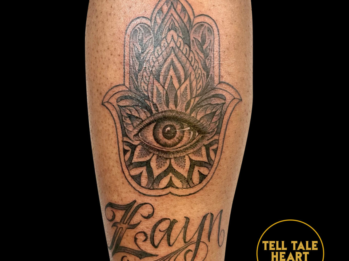 black and grey tattoo of hamsa symbol - a decorative hand shaped design with an eye at the center