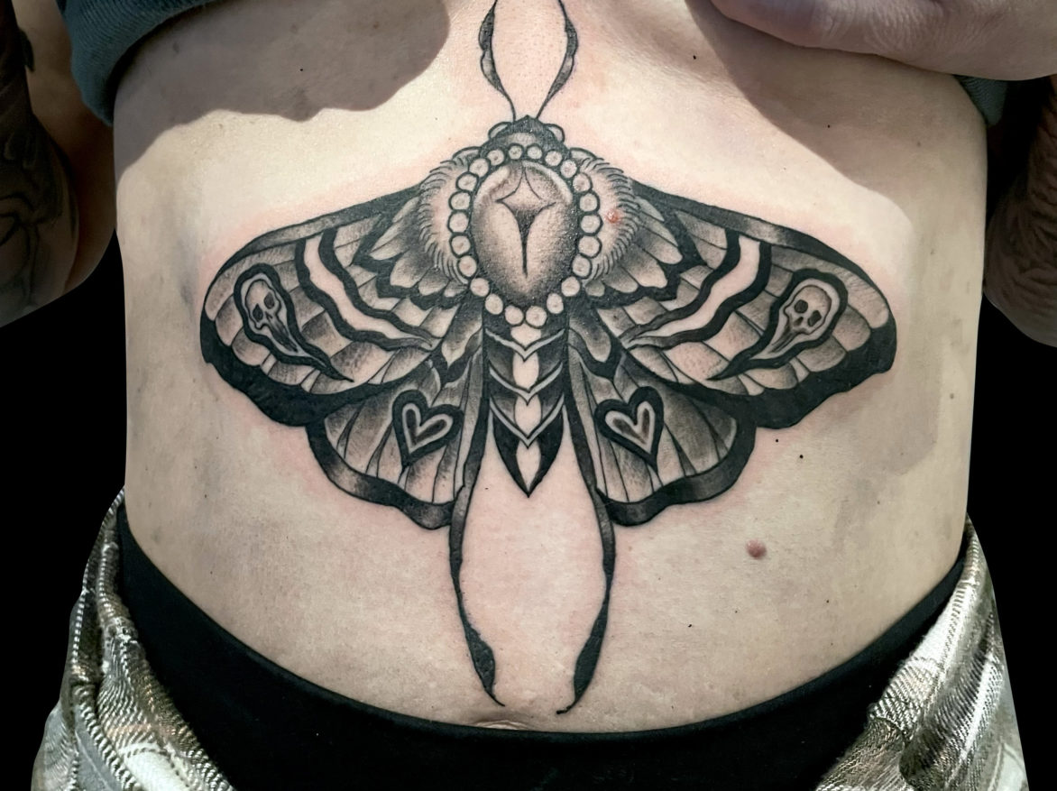 black and grey tattoo of moth on stomach with ghosts and hearts in wing design pattern