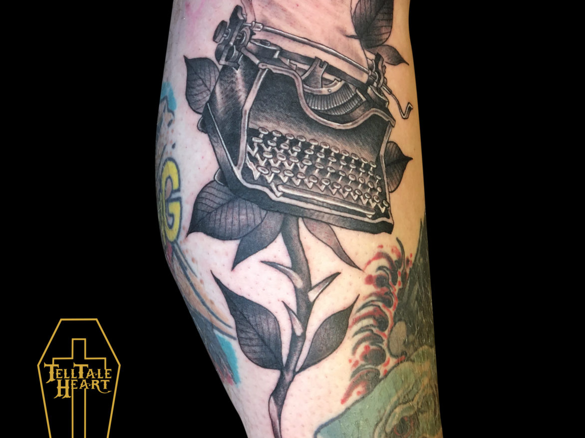 realism tattoo of antique typewriter with a page inside it with a rose stem and leaves underneath