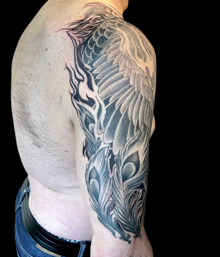 Black and grey tattoo sleeve of phoenix that comes over onto chest with moon in background and negative space flames that go onto the client's back