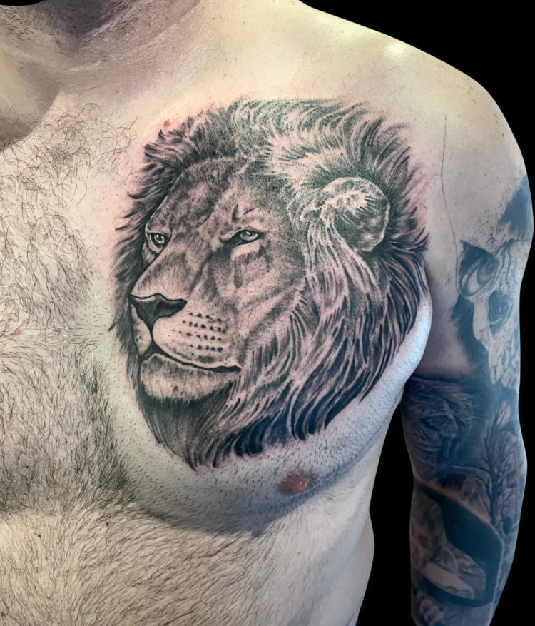 black and grey tattoo of male lion head on left chest