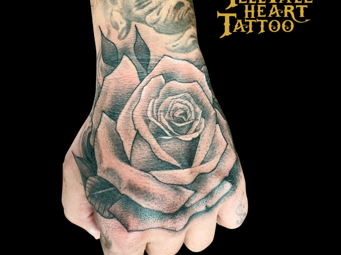black and grey realism tattoo of single rose tattooed on whole hand