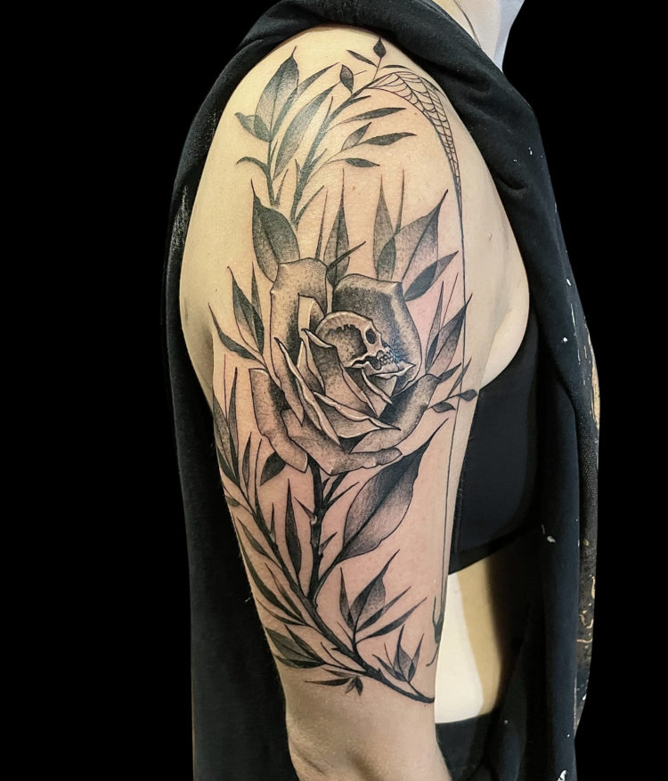 black and grey tattoo sleeve of rose with skull profile at center and lots of long stems, leaves and spider web