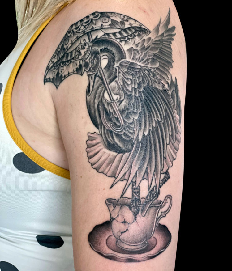black and grey tattoo of black swan wearing a crown holding a parasol inside a broken teacup tattooed on outside shoulder and arm