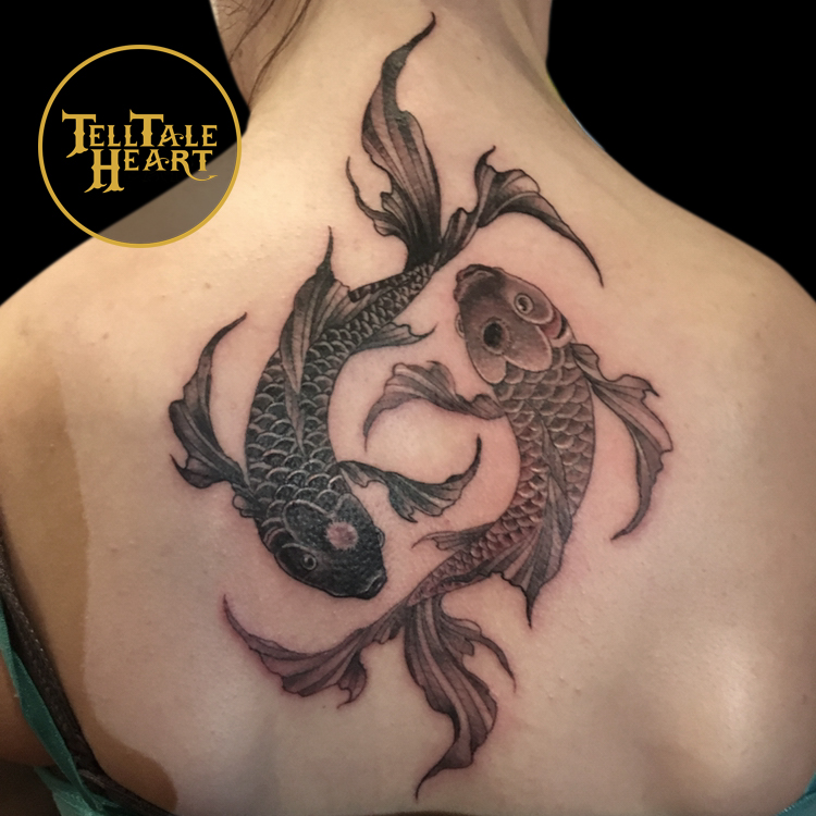 black and grey realism tattoo of two koi fish swimming in a yin yang pattern, one dark, one light, tattooed on a person's back