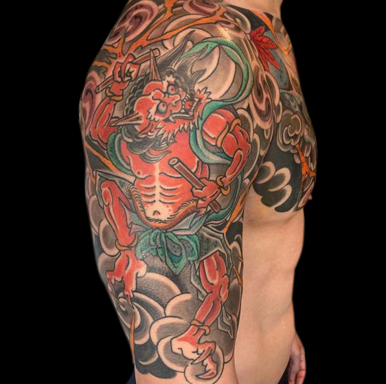 detail of colour Japanese oni samurai warrior tattooed in red wearing green robes looking upward holding wood batons on shoulder