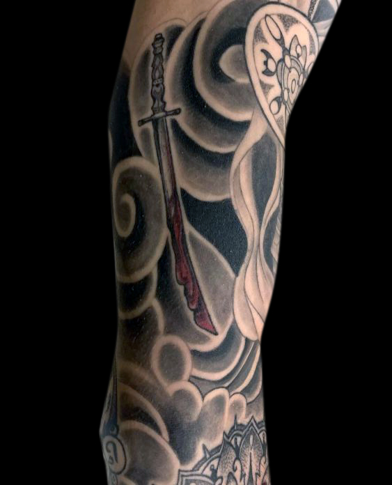 detail of bloody japanese sword tattoo on the inside of bicep surrounded by black and grey wind bars