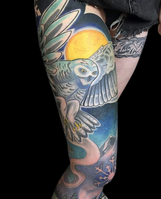 tattoo of owl in flight on upper thigh with moon and starry blue sky in behind and mountains and nature with snowflake on knee