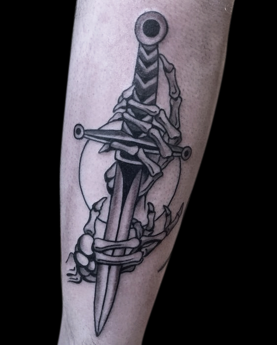 black and grey tattoo of a pair of skeleton hands holding a dagger with a simple circle behind it