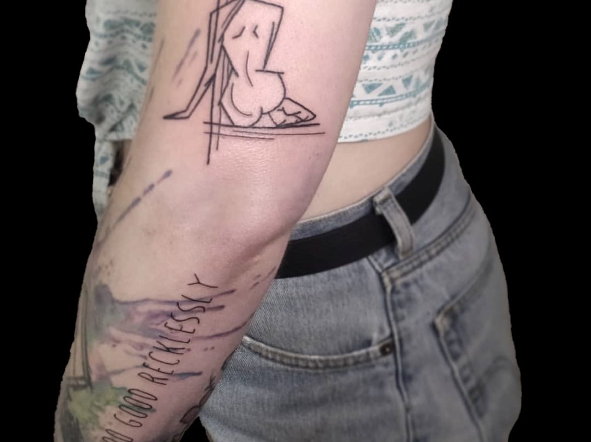 Abstract tattoo of a cubist style drawing of a nude woman with long hair seen from behind sitting on her hip tattooed on back of arm just above the elbow