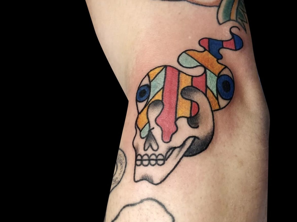 abstract colour tattoo of a skull with a plume of geometic colourful smoke coming from its eyes tattooed on side of elbow