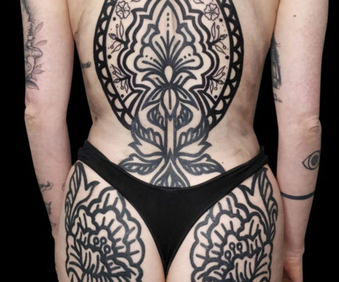 large blackwork ornamental design of flowers on entire back and buttocks solid thick black lines no shading