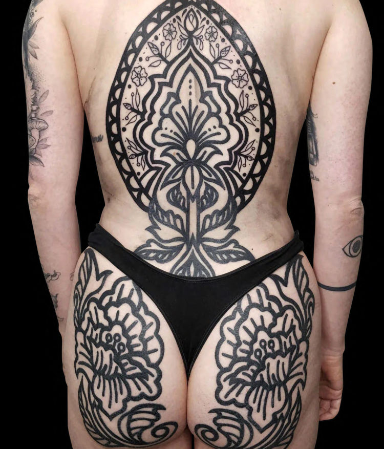 large blackwork ornamental design of flowers on entire back and buttocks solid thick black lines no shading