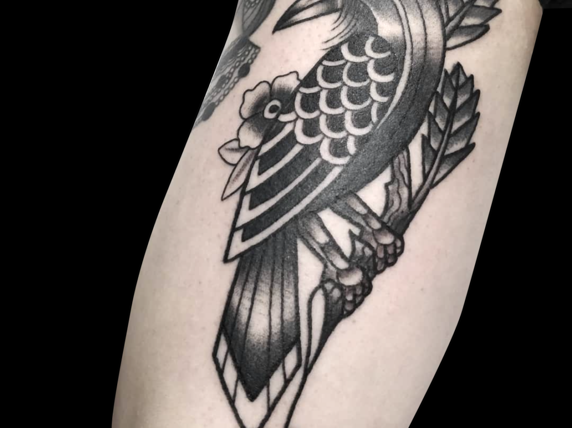 black and grey tattoo of simplified bird on a branch with two flowers behind it