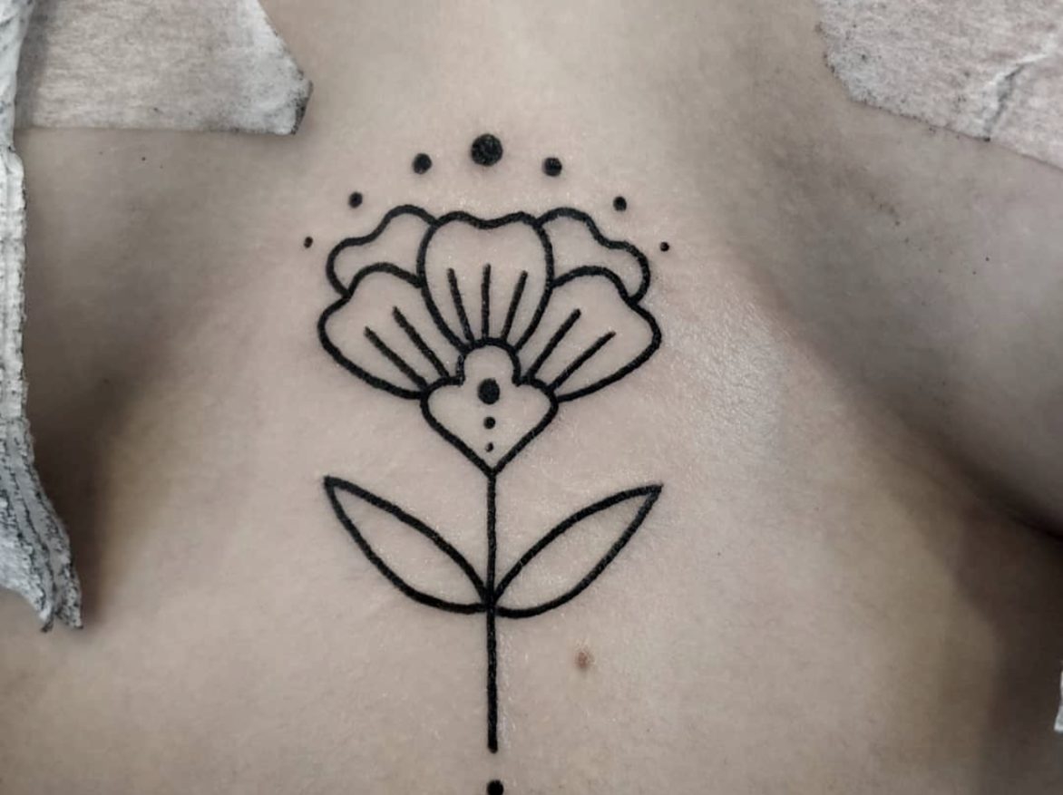 simple blackwork flower tattoo single flower with two leaves and stem and ornamental dots tattooed on sternum