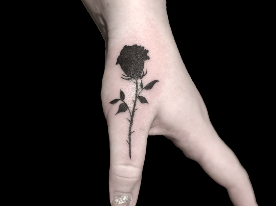 blackwork tattoo of single solid black rose on thumb