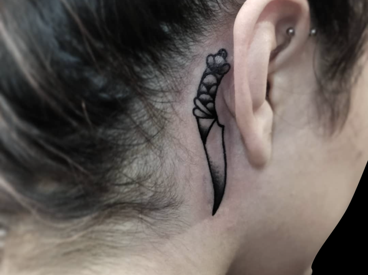 traditional tattoo of dagger in black and grey tattooed behind ear