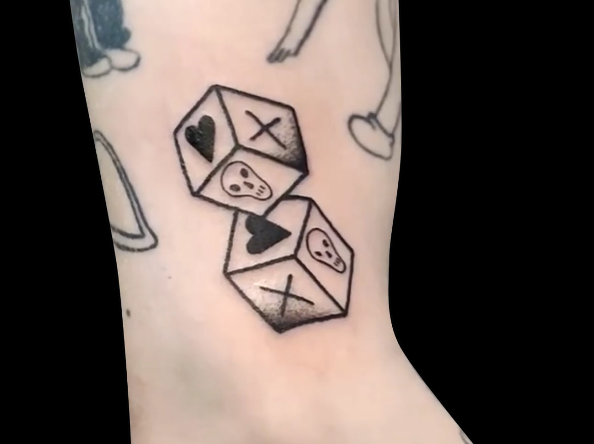 blackwork tattoo of a pair of dice with simple hearts, skulls and x's instead of number dots tattooed on side of arm just above elbow