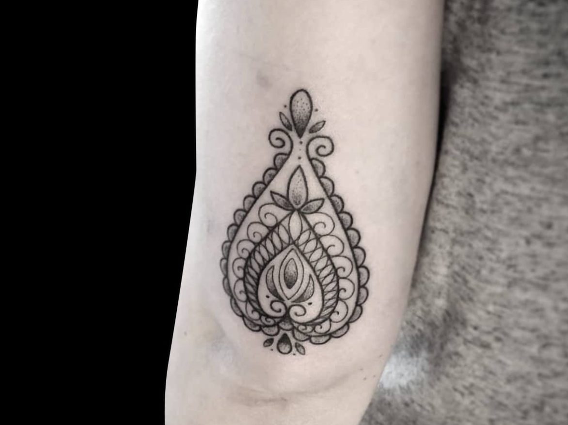 fineline ornamental tattoo of a single paisley design on back of arm just above elbow shaded with dotwork