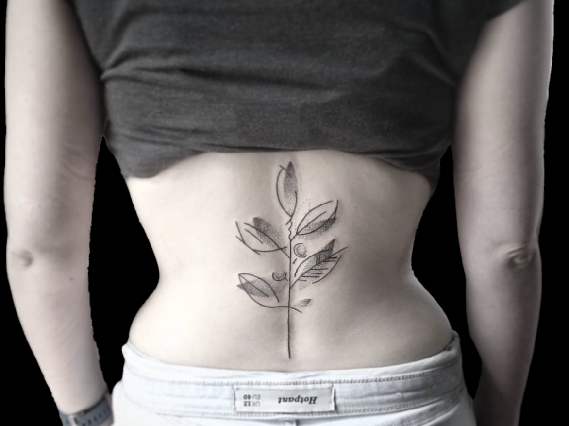 tattoo of illustrative abstract flower tattooed on the lower back along spine. Single flower with four leaves and simple stem