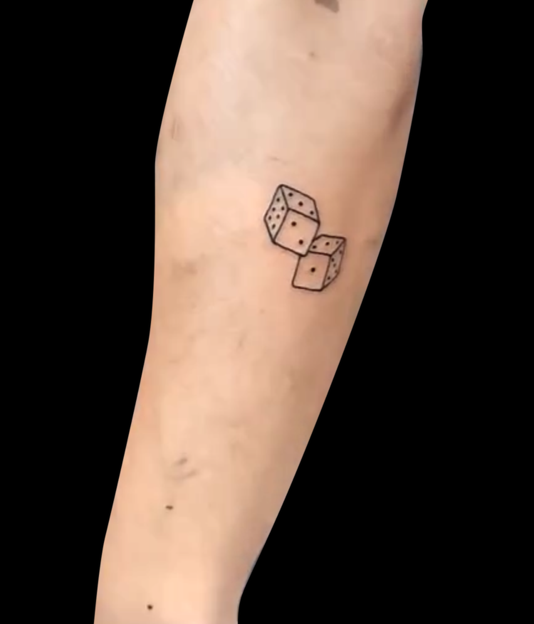 fineline tattoo of a pair of dice done in black ink with simple outline tattoed on back of forearm just below elbow