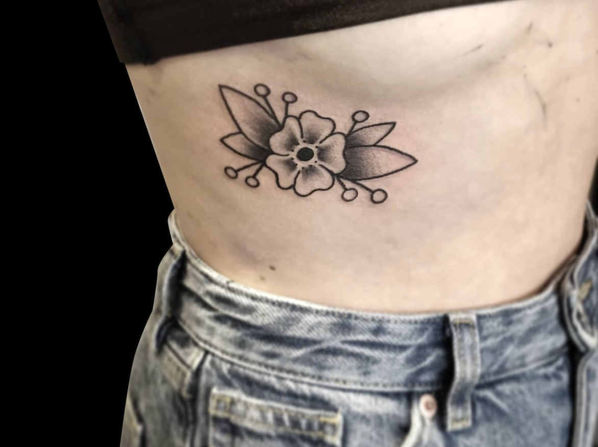 traditional tattoo of single cherry blossom flower with leaves tattooed in black and grey on side of ribs