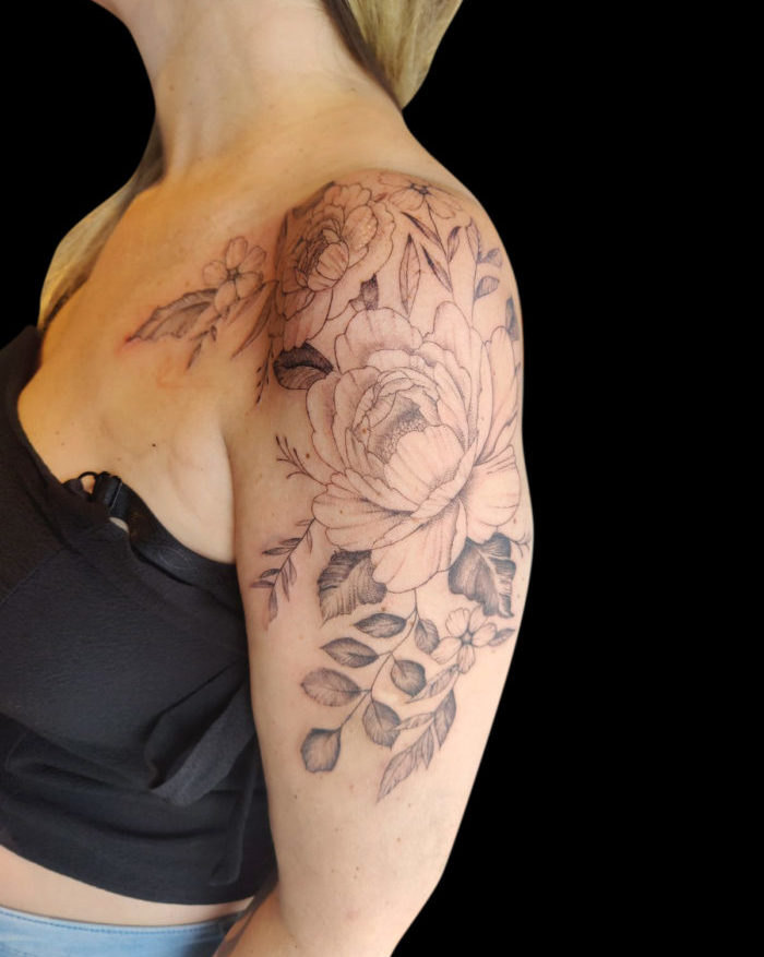 fineline floral tattoo of flowers on shoulder and leaves spreading down arm and front of chest