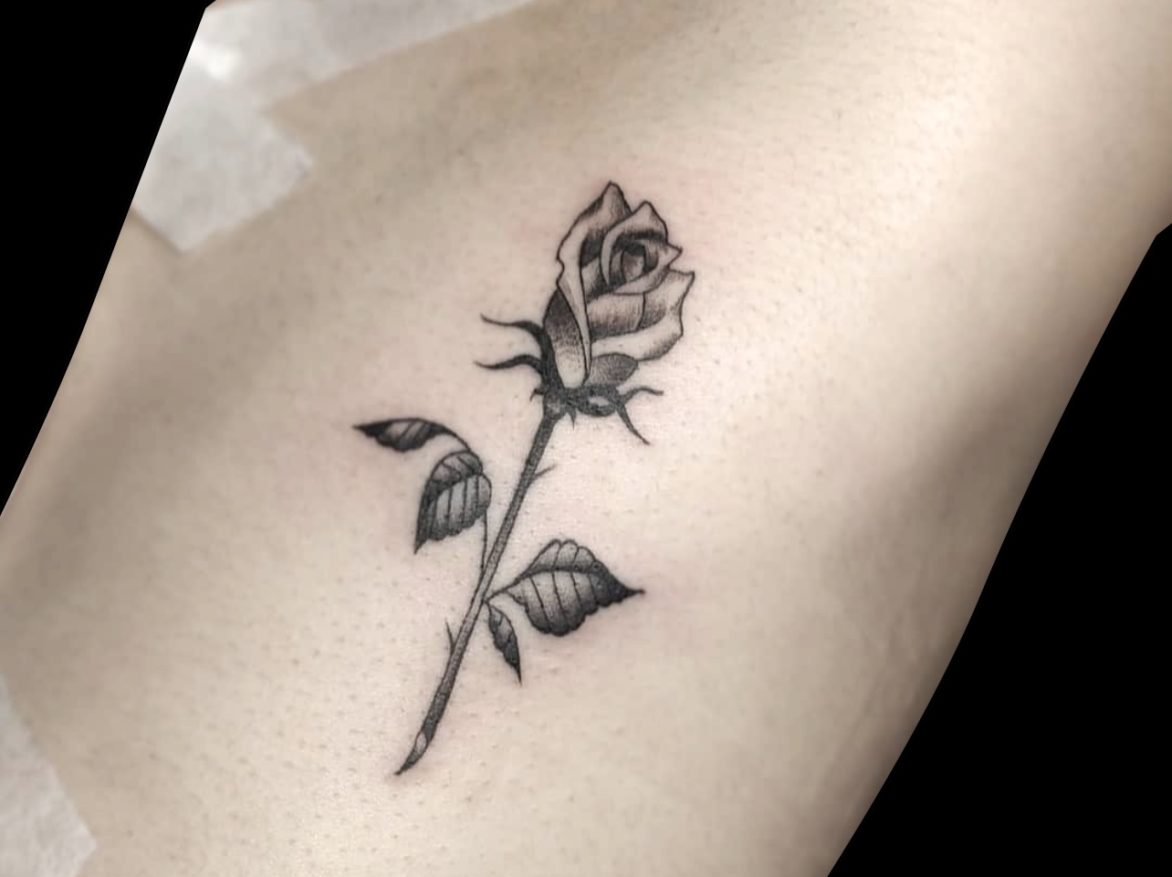 fineline tattoo of a simple rose with two leaves and thorns
