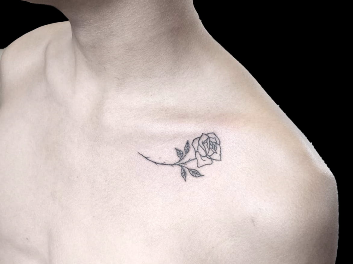 fineline tattoo of a single back rose just below left collar bone