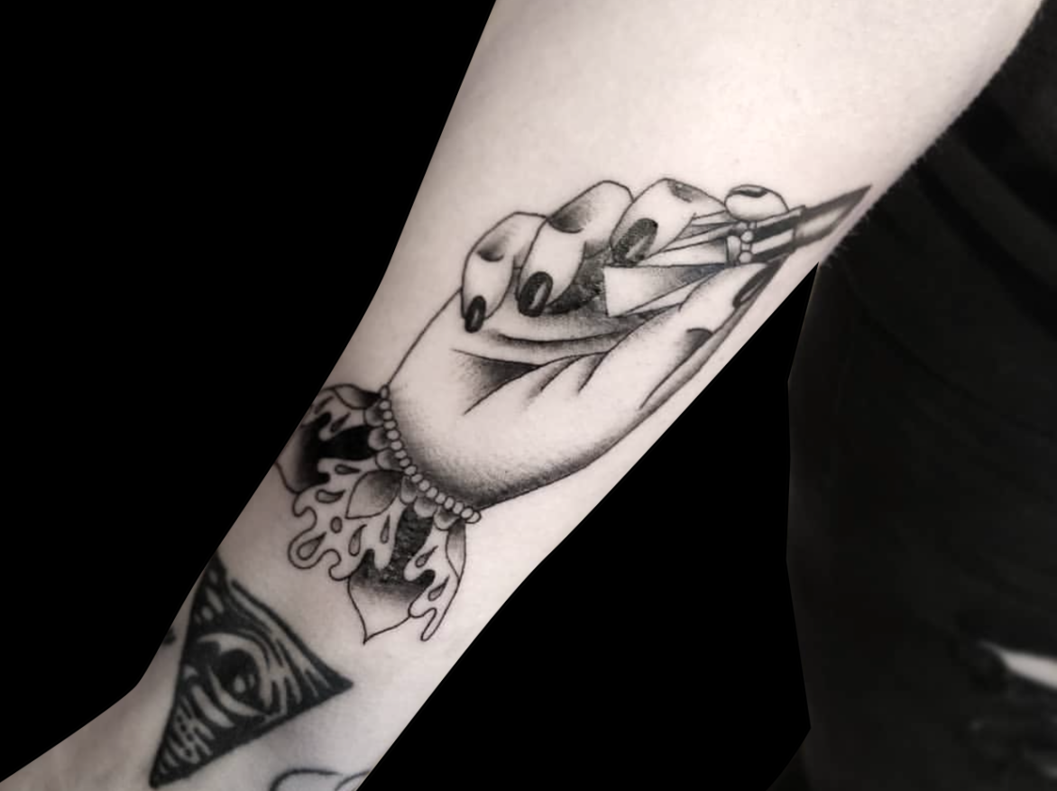 black and grey tattoo of a hand with painted fingernails holding a tube of open lipstick with elegant wrist cuff