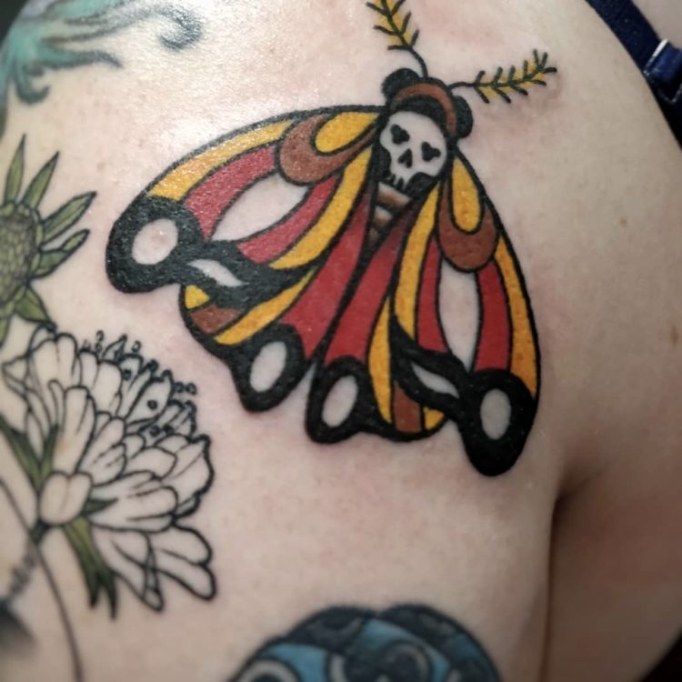 traditional tattoo of death head moth with yellow, red and black wings on front of shoulder