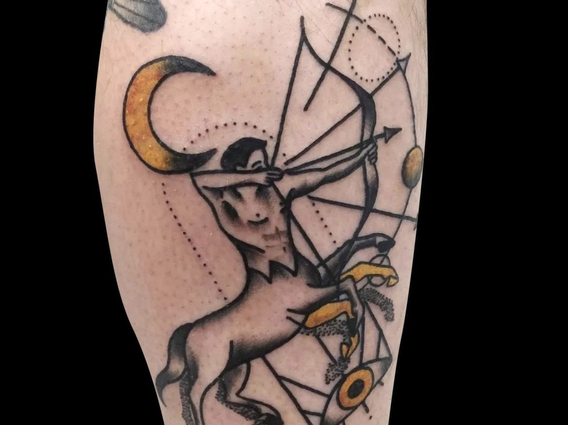 saggitarius archer tattoo of half horse half man holding bow and arrow with yellow moon and eye motif on side of calf