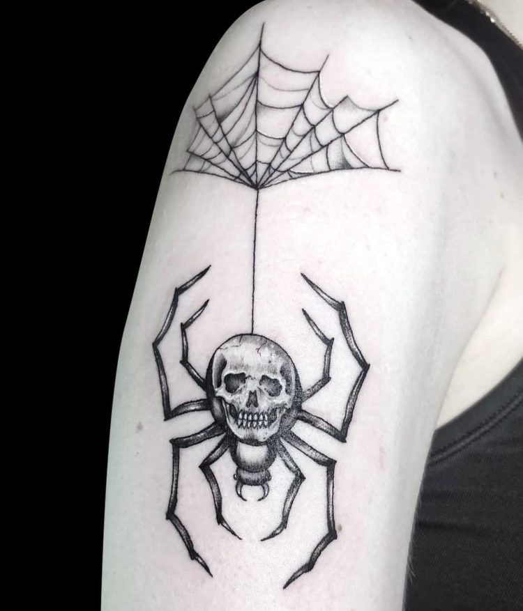 black work tattoo of a large spider with a skull for a body hanging from a cowbweb tattooed on right shoulder