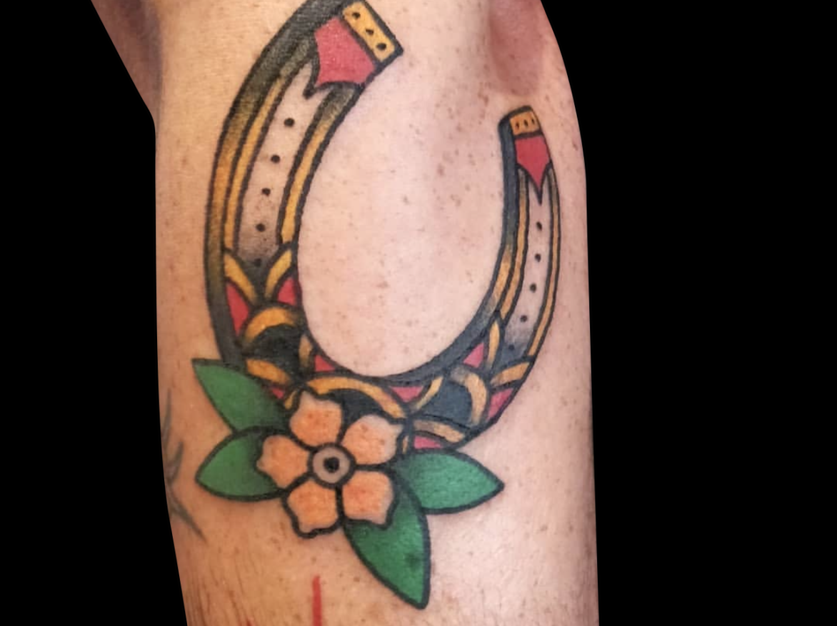 traditional tattoo of horseshoe with a single yellow flower and green petals tattooed on side of forearm