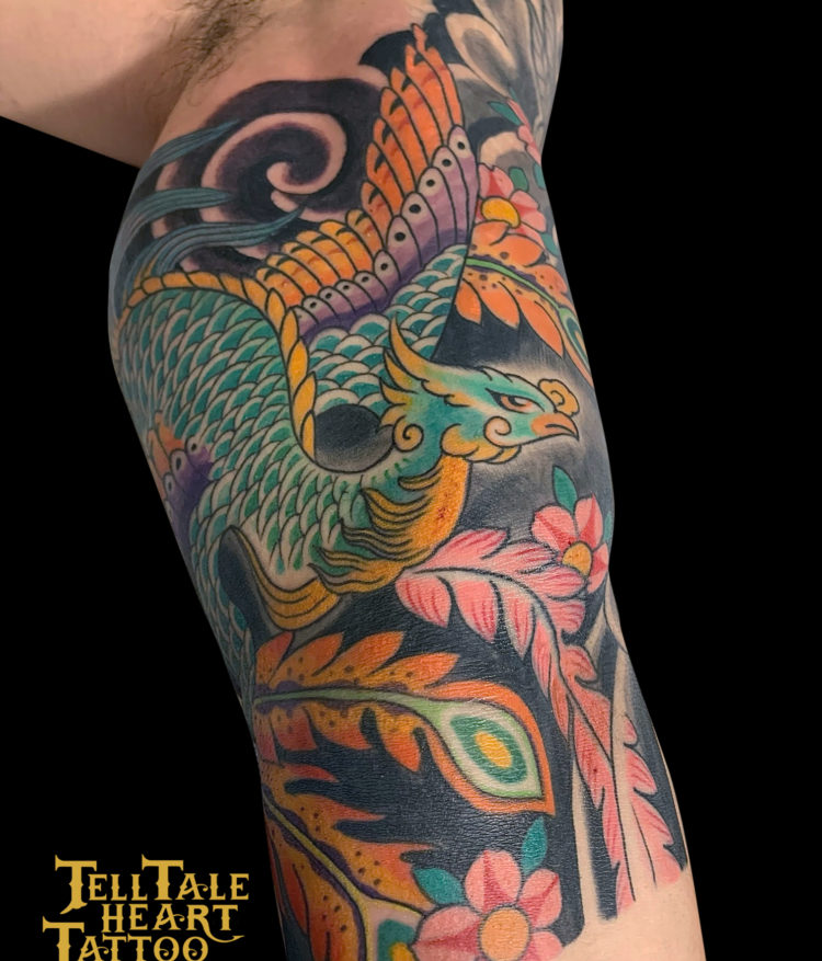 Colour Japanese tattoo detail of green and orange phoenix on inside of arm with cherry blossoms and wind bars