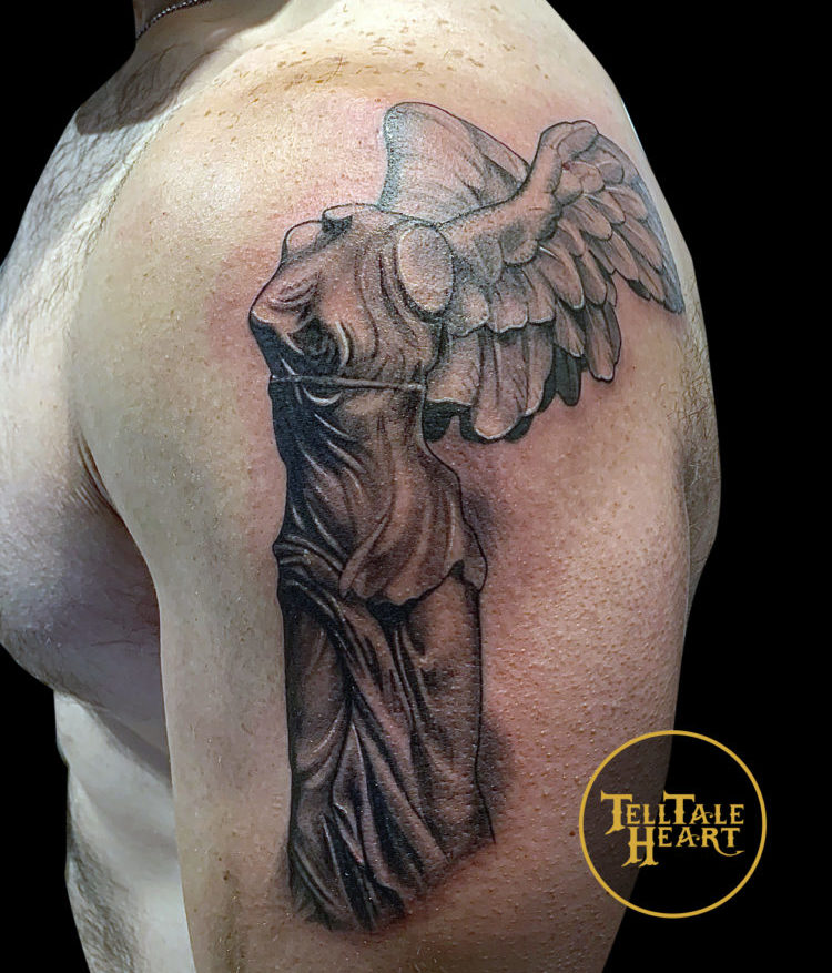 black and grey tattoo of sculpture called Winged Victory of Samothrace depicting a headless and armless robed figure with angel wings tattooed on left shoulder