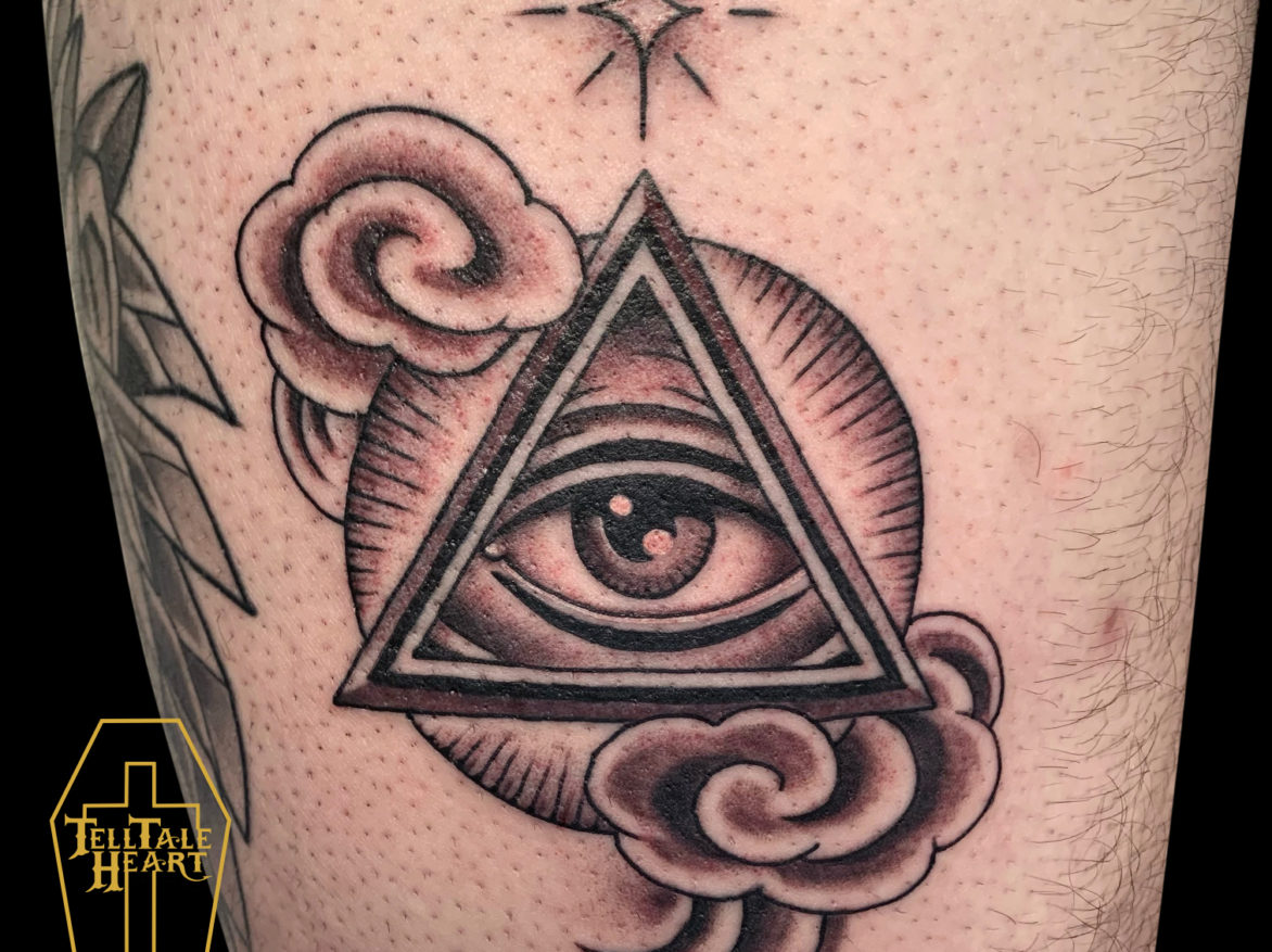 black and grey tattoo of an all seeing eye in the middle of triangle, with sylized clouds around it and a twinkly star above