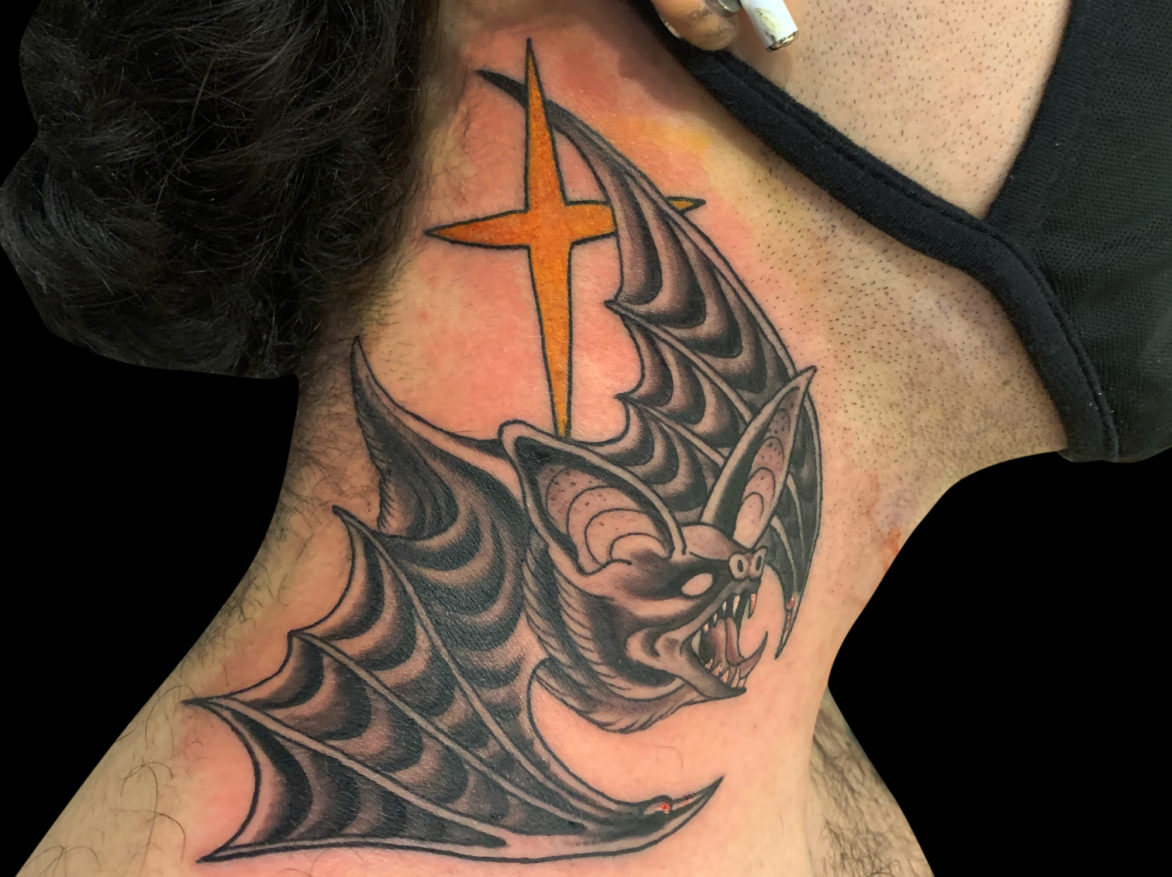 black and grey tattoo of a flying black bat on the side of neck with a yellow star
