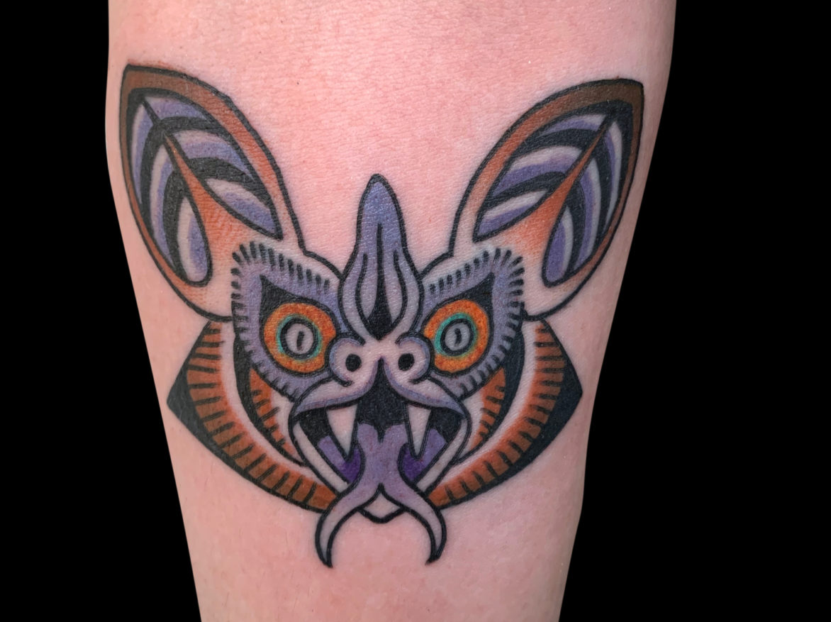 stylized tattoo of a purple and brown bat head with a split tongue and fangs beared