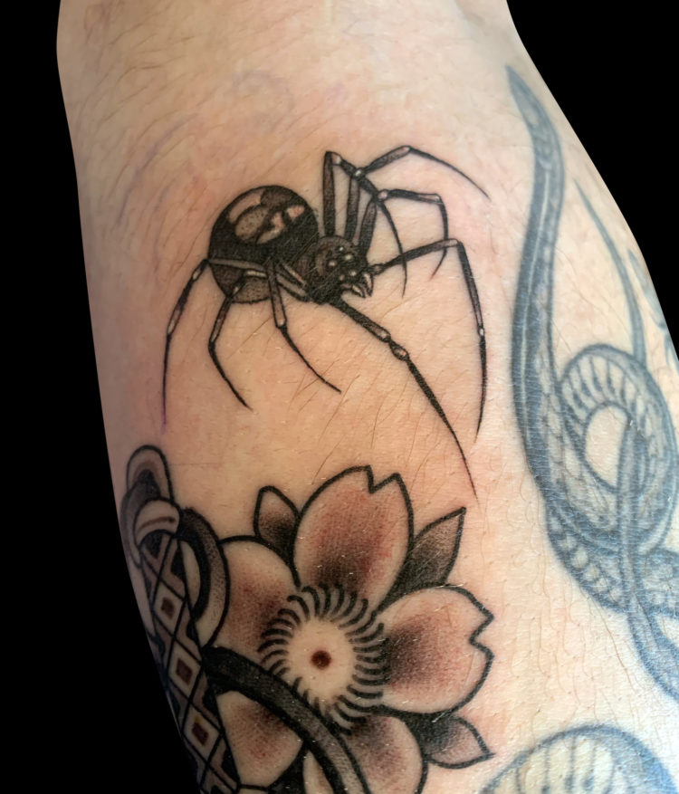 realism tattoo of a back widow spider crawling on a forearm