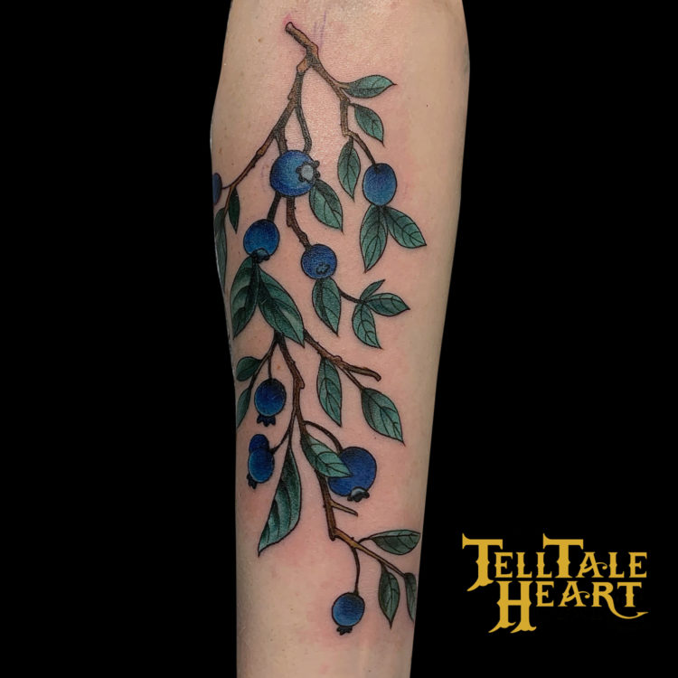 colour tattoo of a blueberry branch with nine blueberries and lots of little green leaves traveling downward on back of leg