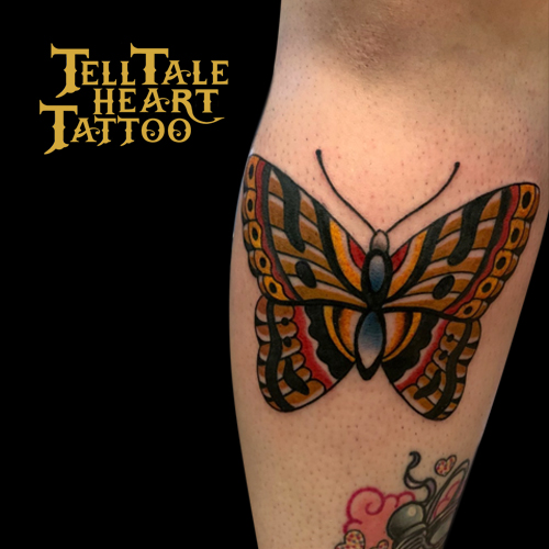 Traditional colour butterfly tattoo with orange, brown, red and blue tattooed on back of calf