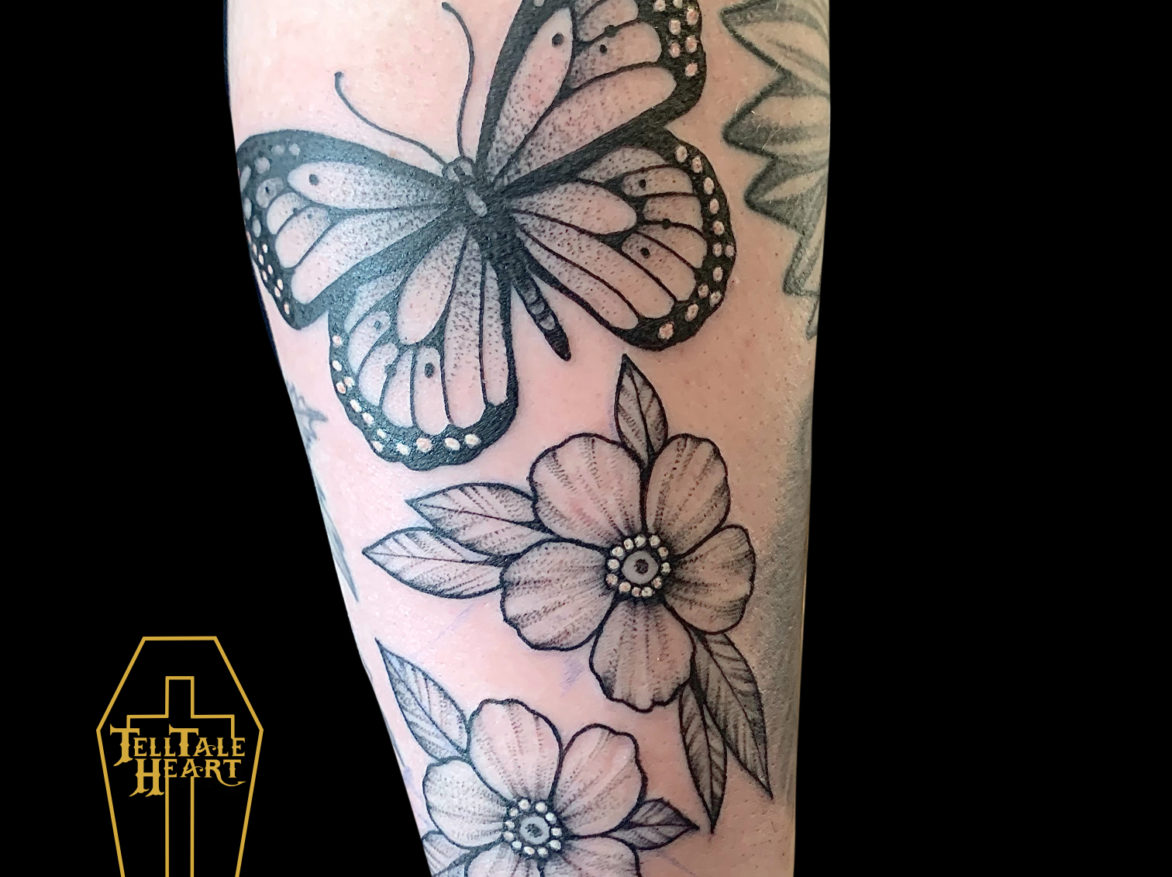 blackwork tattoo of a large monarch butterfly with two small flowers below it on forearm