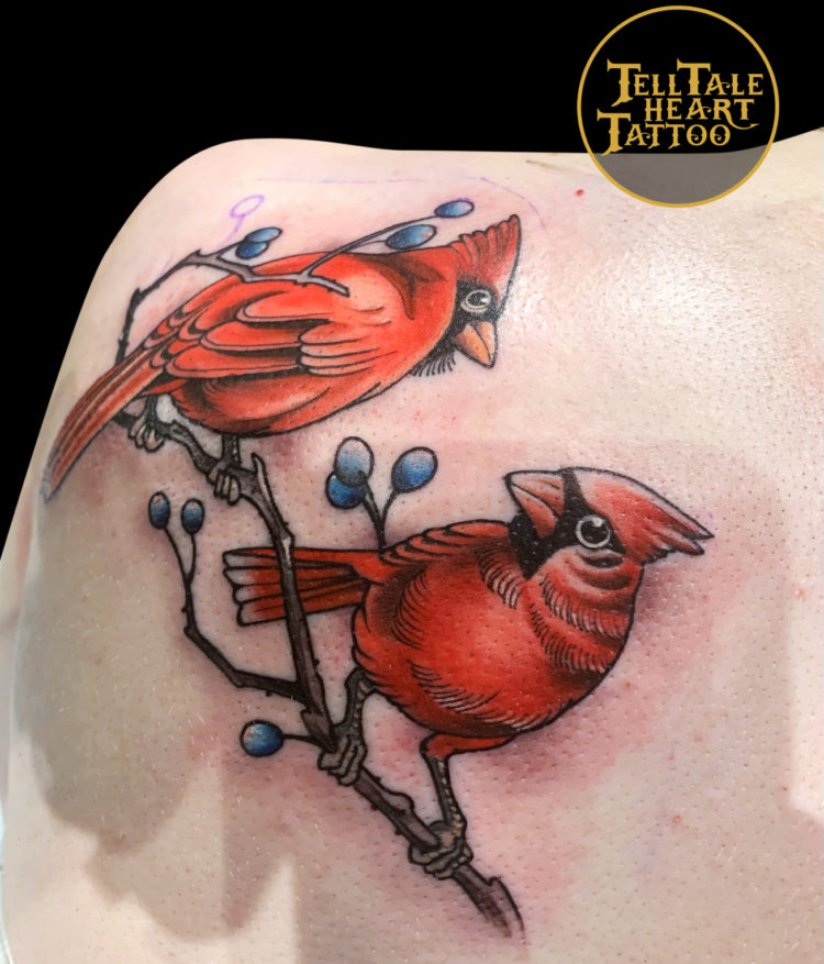 illustrative colour tattoo of two red cardinals perched on a blueberry branch looking at each other tattooed on the back of shoulder