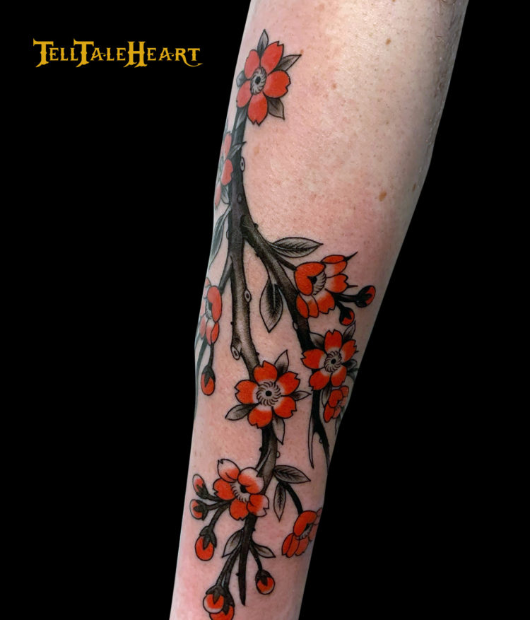 tattoo of a cherry blossom branch with red petals and a black and grey stem on a forearm