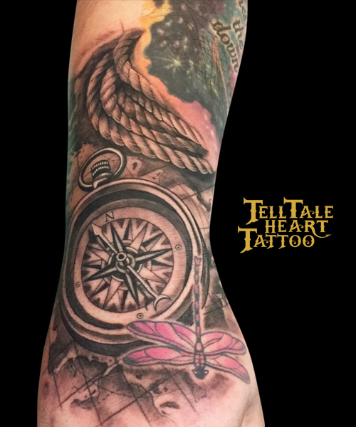 black and grey compass tattooed on the top of the hand, with loops of rope abive and a map below along with a pink dragonfly